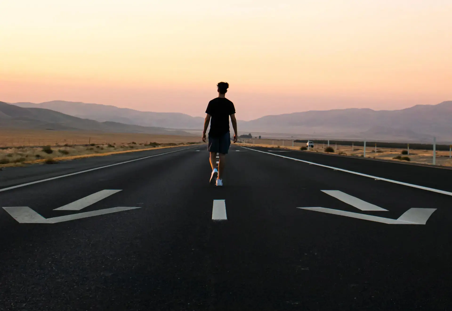 Man on highway walking opposite of directional arrows